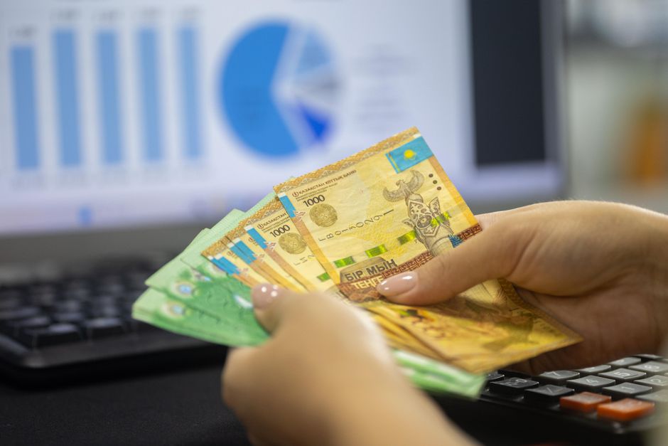 Ruke koje drže novčanice s financijskim grafovima na ekranu računala
