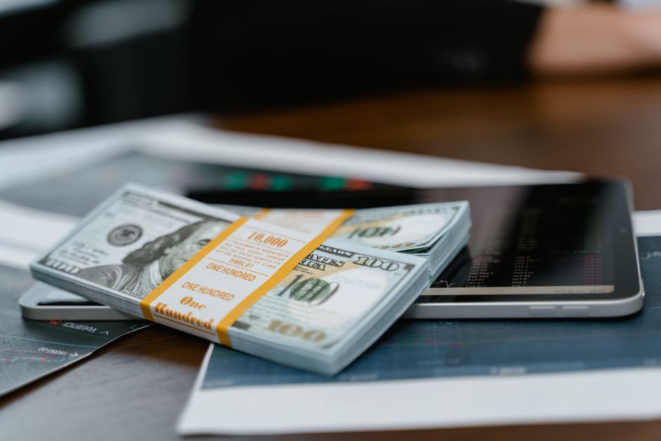 Stog novčanica od 100 dolara na tabletu s financijskim grafikonima
